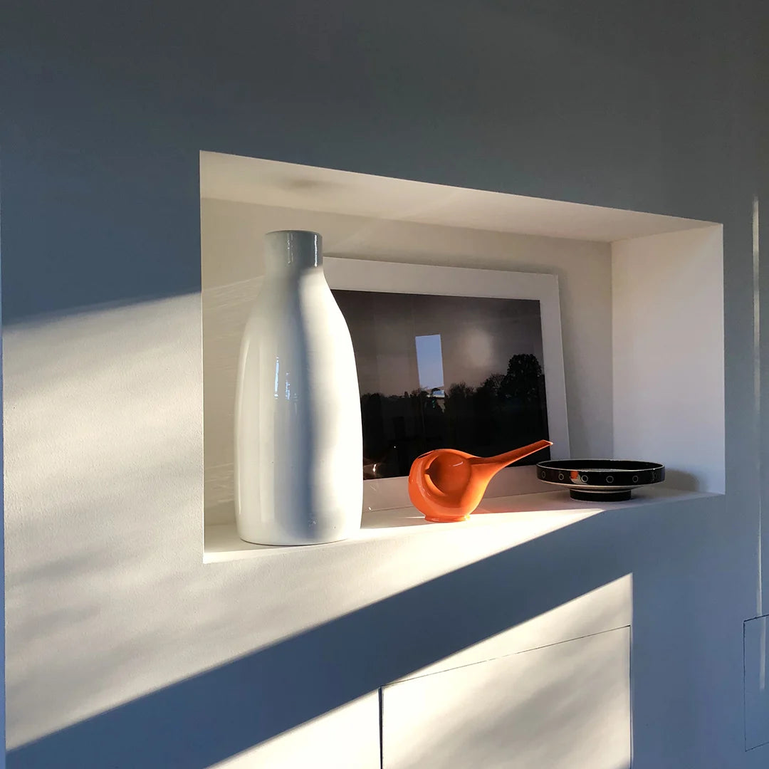 Eine orange Gießkanne auf einem weißen Regal im Sonnenlicht